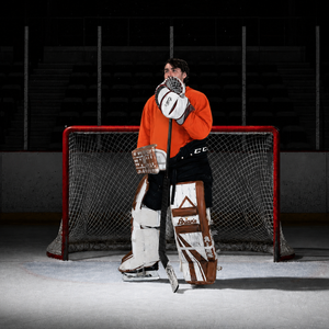 Goal Keeper standing in front of hockey goal wearing pads and gloves.
