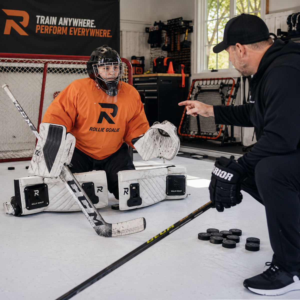 Hockey player in orange jersey with 'Rollie Goalie' branding receiving instruction from a coach in a garage setting.